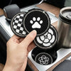 A hand holds three round coasters with different patterns, including a black and white checkered design and a paw print.