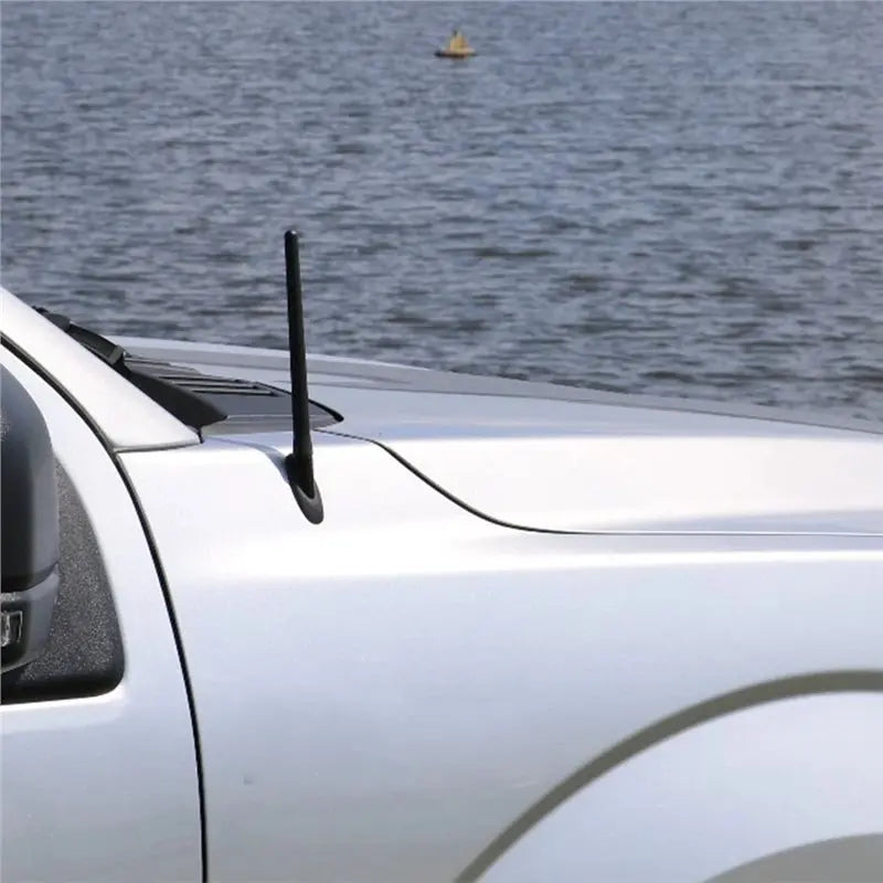 A close-up of a black replacement antenna mast mounted on the roof of a white Ford F-150 truck.