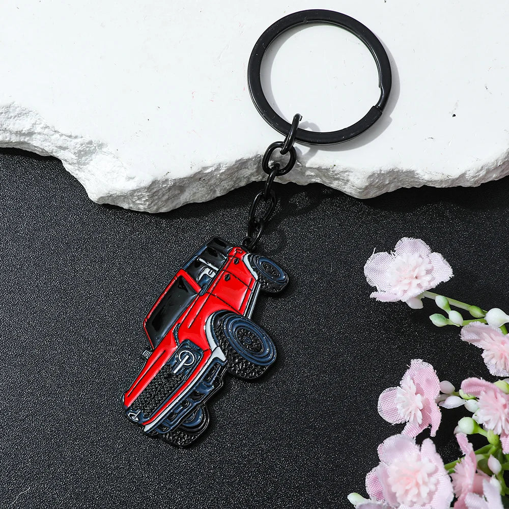A red classic alloy car keychain with a silver emblem and black rubber tires, displayed on a dark surface.
