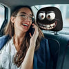 A woman is using a cell phone while sitting in a car, with a black cartoon face headrest cover visible.
