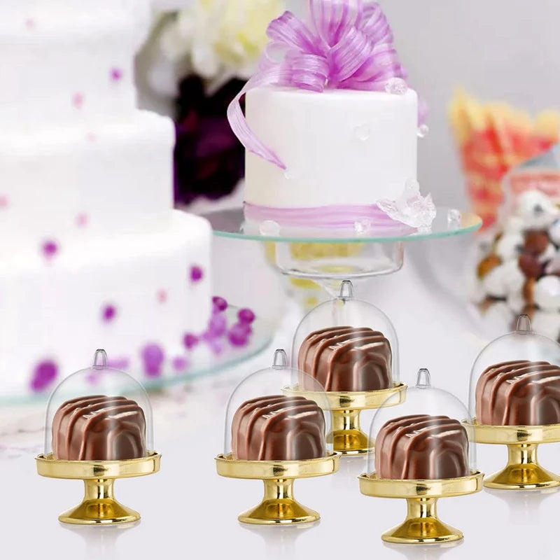 Präsentation von Mini-Schokoladencupcakes in klaren Glasdomen auf goldenen Ständern mit einem weißen Kuchen im Hintergrund
