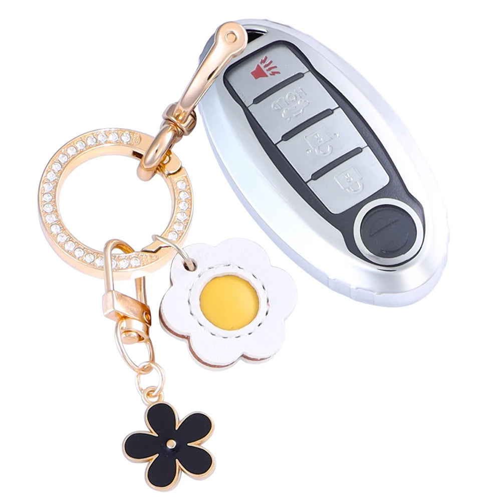 A silver car key fob cover with a gold chain and a flower charm attached.